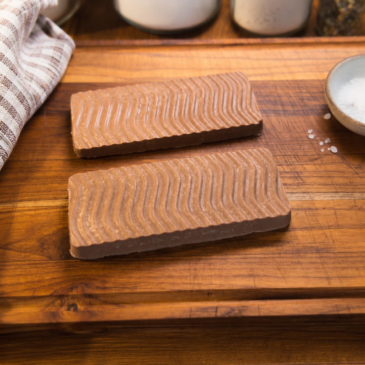 Homemade healthy chocolate bars made with protein powder, coconut oil, peanut butter, and honey, resting on a rustic wooden cutting board with a farmhouse kitchen towel.