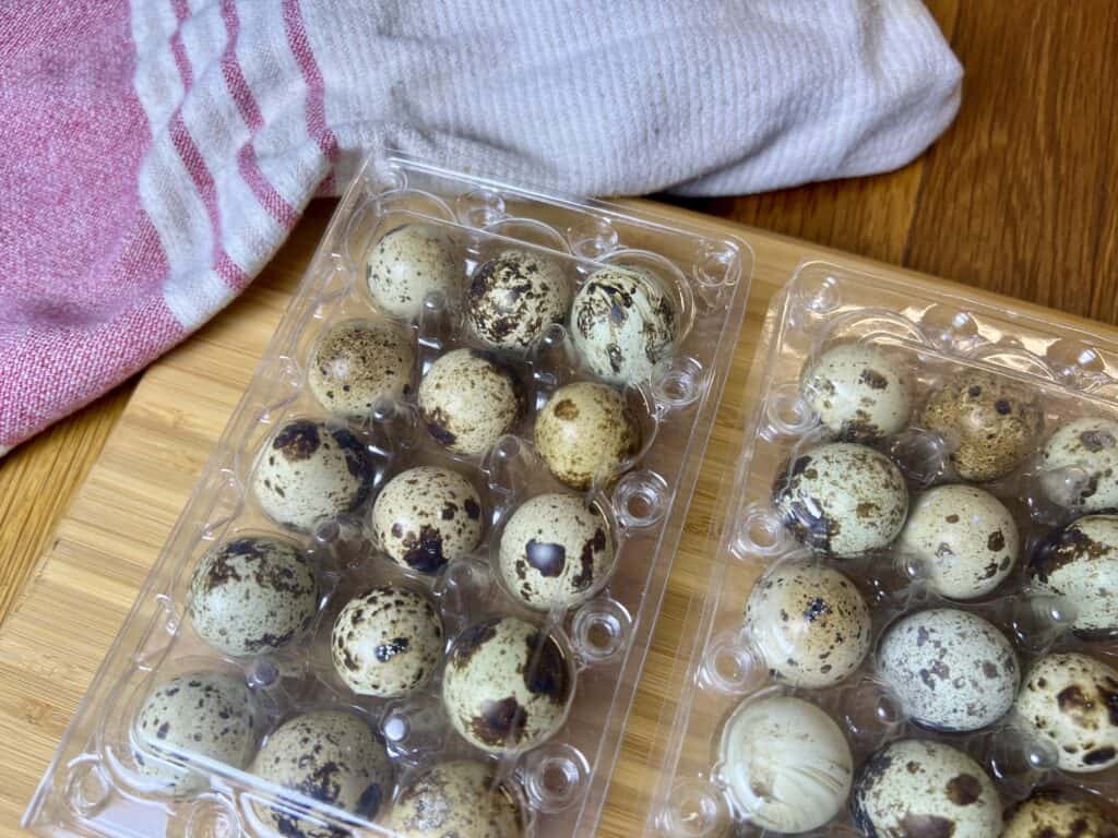 two cartons of quail eggs on top of a cutting board. 