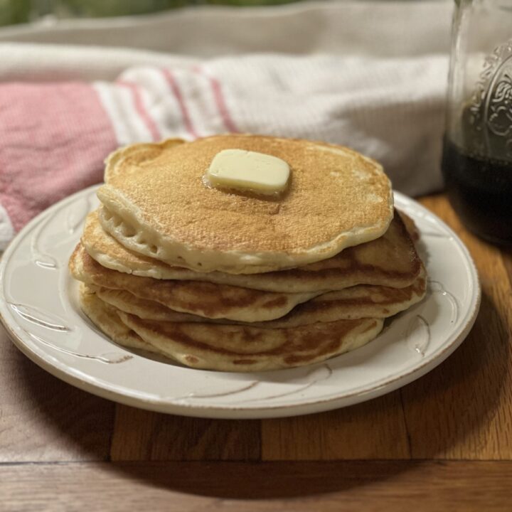 stacked sourdough pancakes on a plate with butter on top and ready to eat.