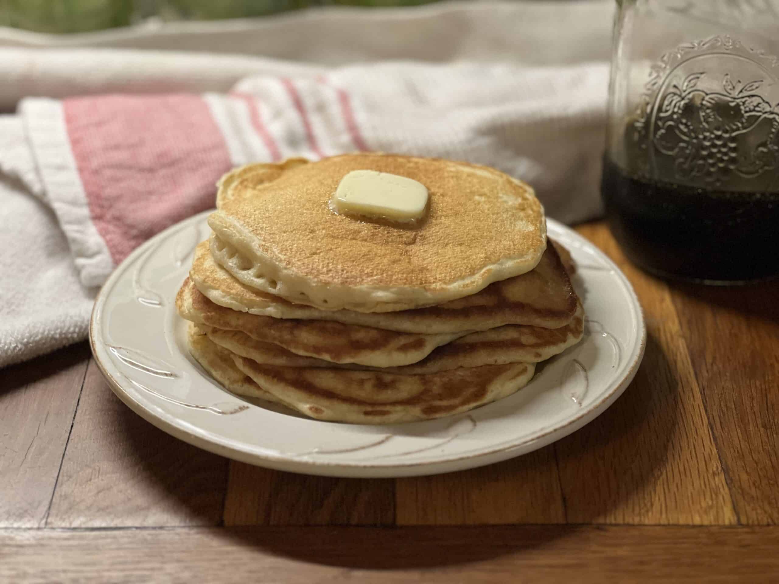 stacked sourdough pancakes on a plate with butter on top and ready to eat.