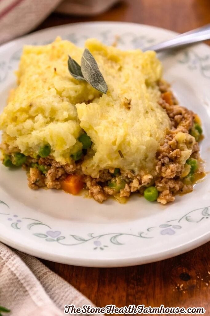 Serving of homemade rabbit shepherd’s pie with mashed potatoes, peas, and carrots on a vintage plate