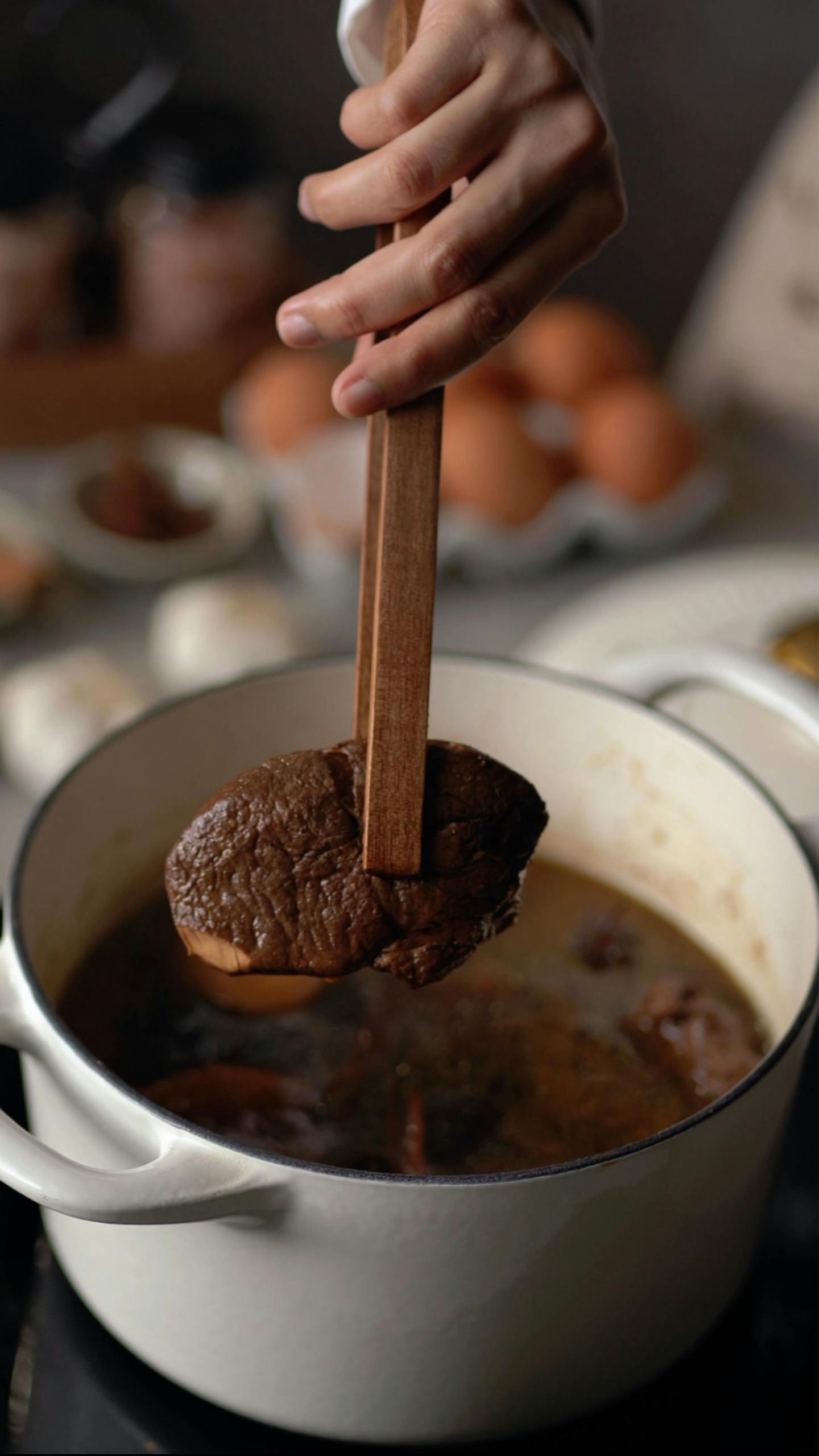 Close-up of hand cooking rich meat stew in pot, depicting home-cooked meal preparation.