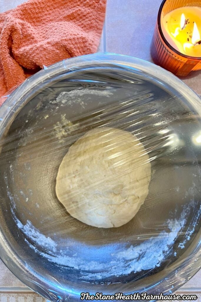 Sourdough cinnamon roll dough resting in a covered glass mixing bowl