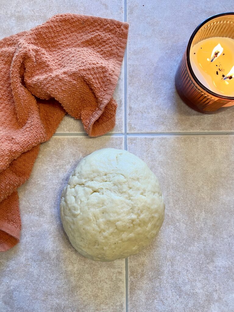 Homemade sourdough cinnamon roll dough ball resting on a tiled counter top before rising.