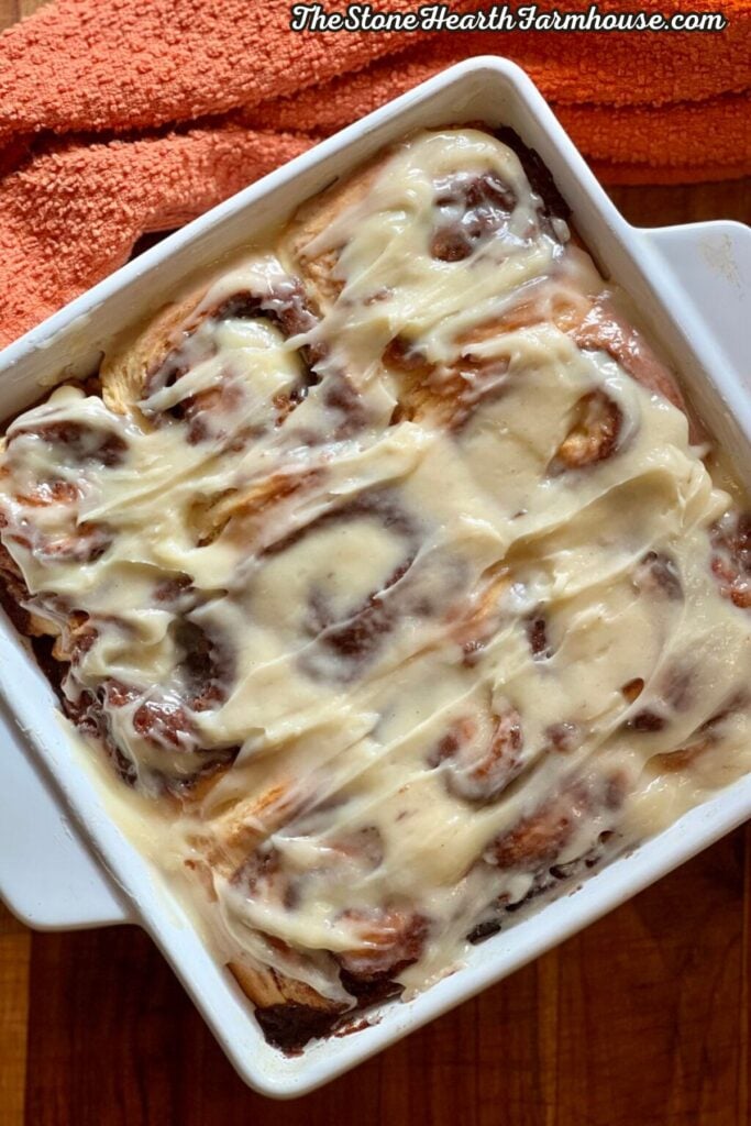 Sourdough cinnamon rolls topped with creamy cream cheese frosting in a white baking dish