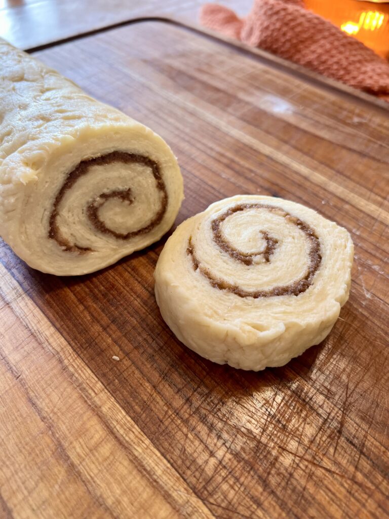 Slice of sourdough cinnamon roll dough showing spiral layers of cinnamon sugar filling on a wooden cutting board.