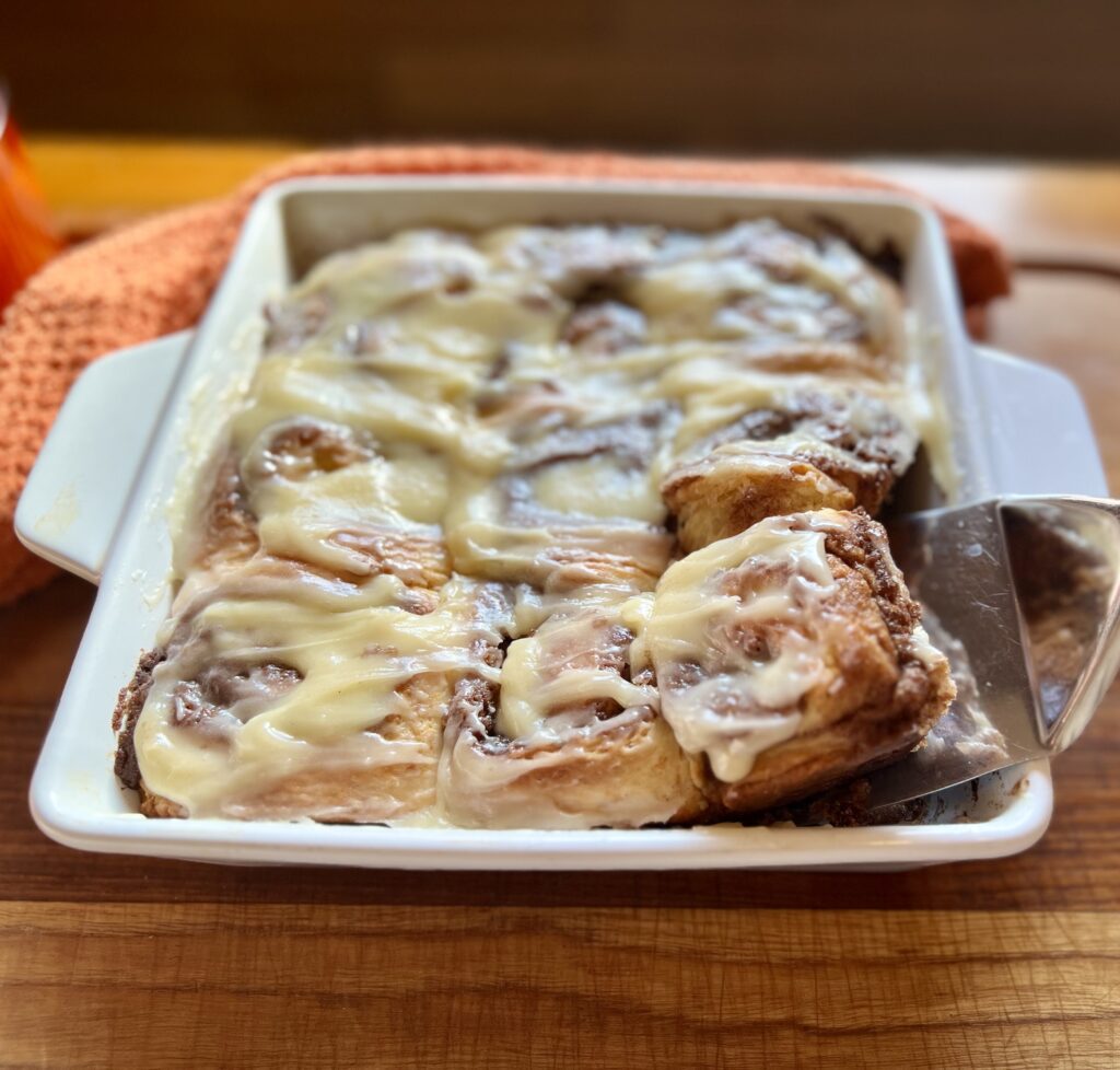 Easy overnight sourdough cinnamon rolls topped with cream cheese icing, with one roll being lifted from the baking dish.