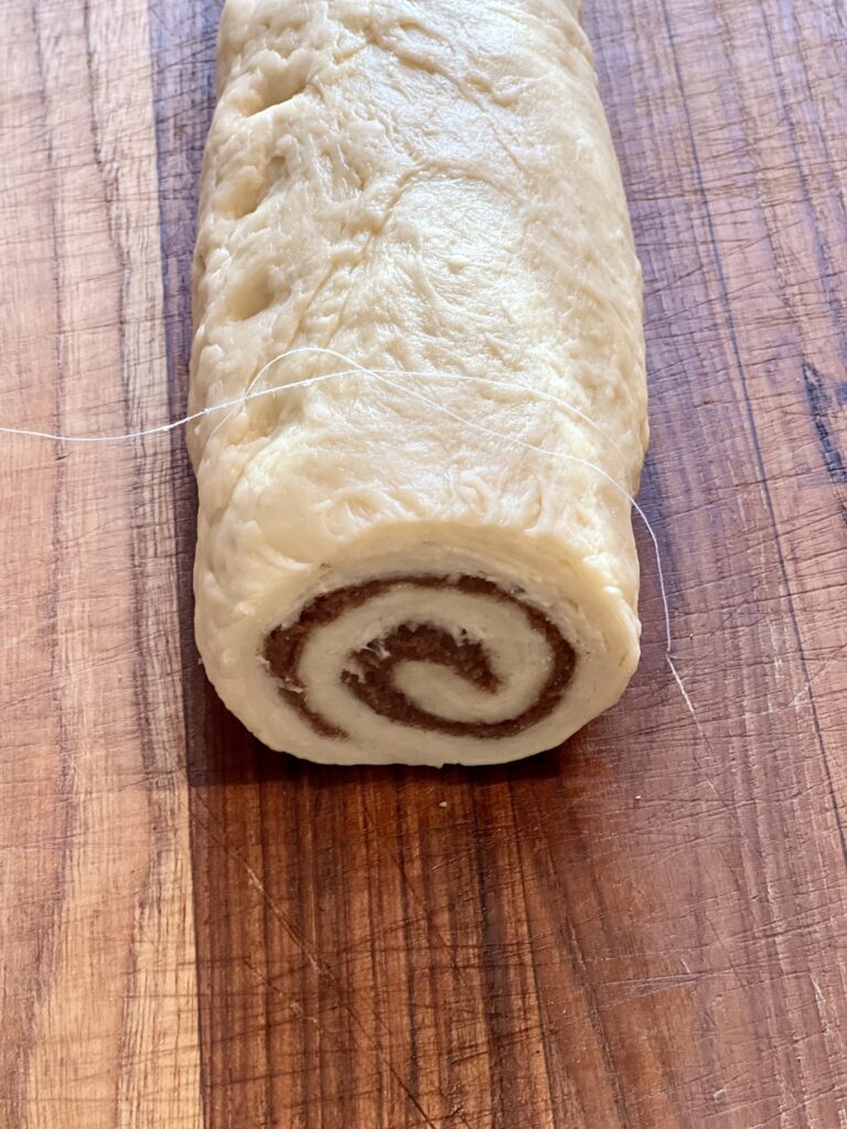 Sourdough cinnamon roll dough log filled with brown sugar and cinnamon, ready to be sliced before baking.
