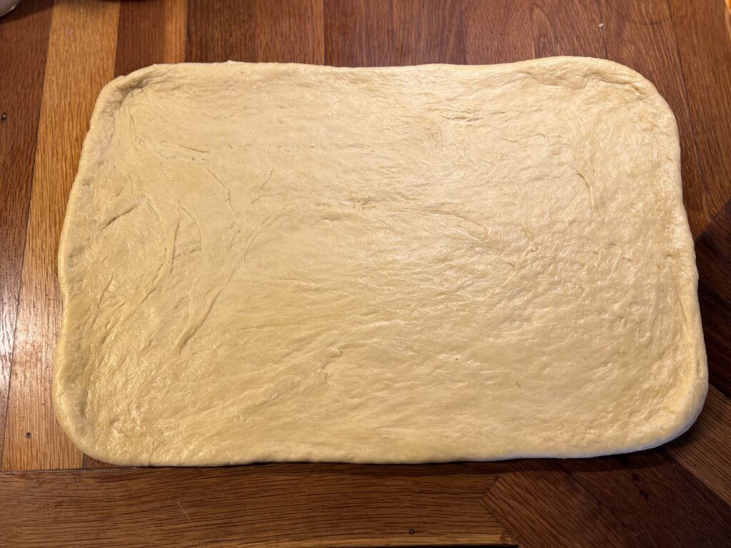 Soft sourdough dough rolled into a rectangle on a wooden surface, ready for cinnamon sugar filling.