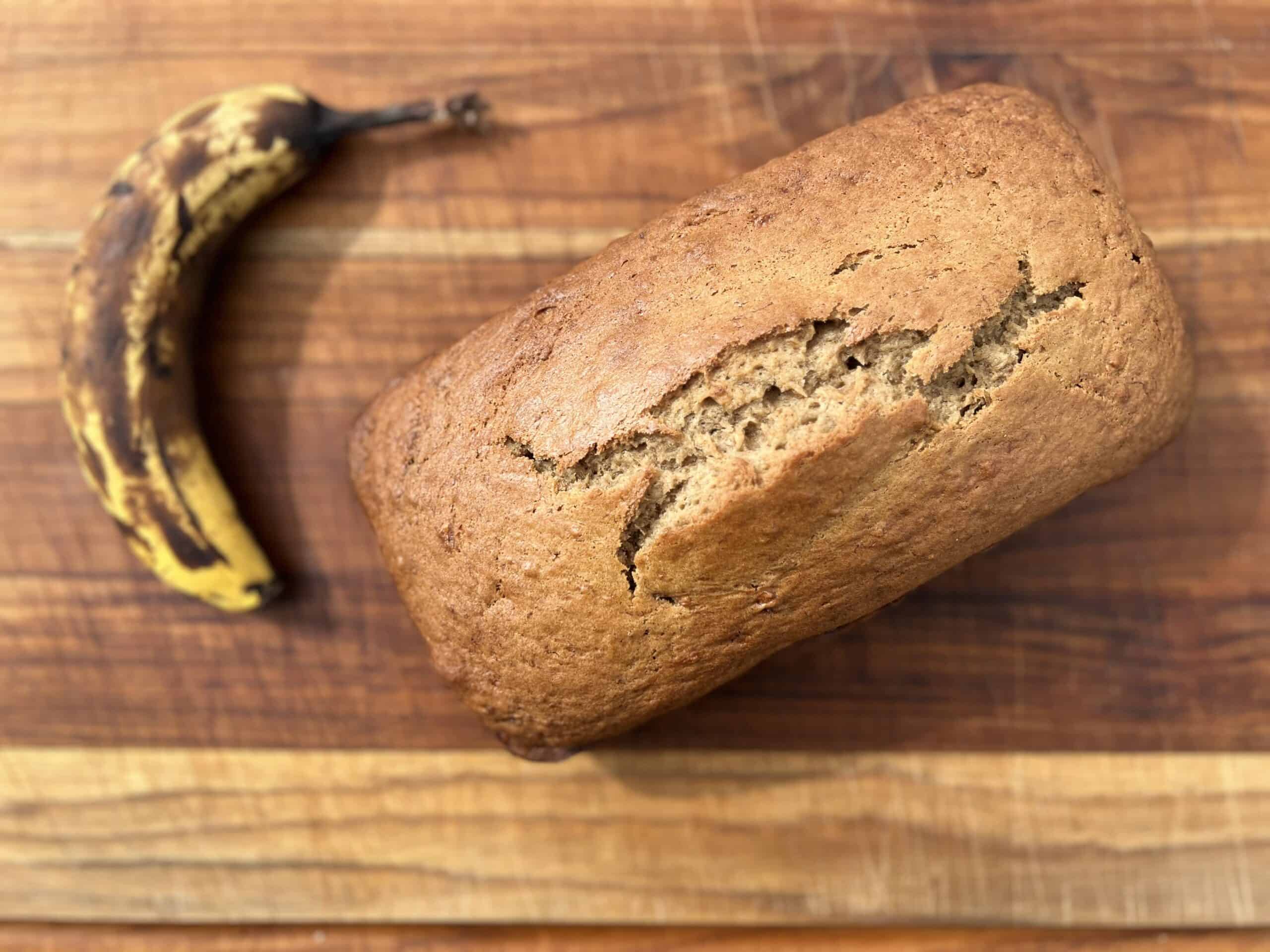 banana bread on a wooden cutting board with a ripe banana