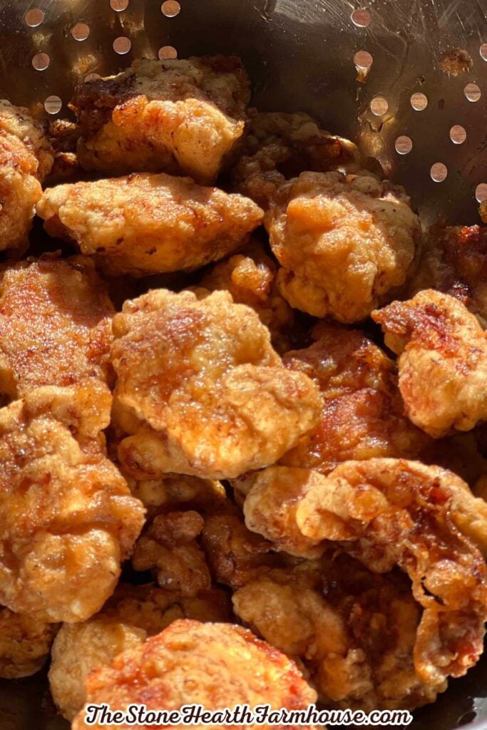 Golden brown pieces of fried rabbit meat draining in a metal colander