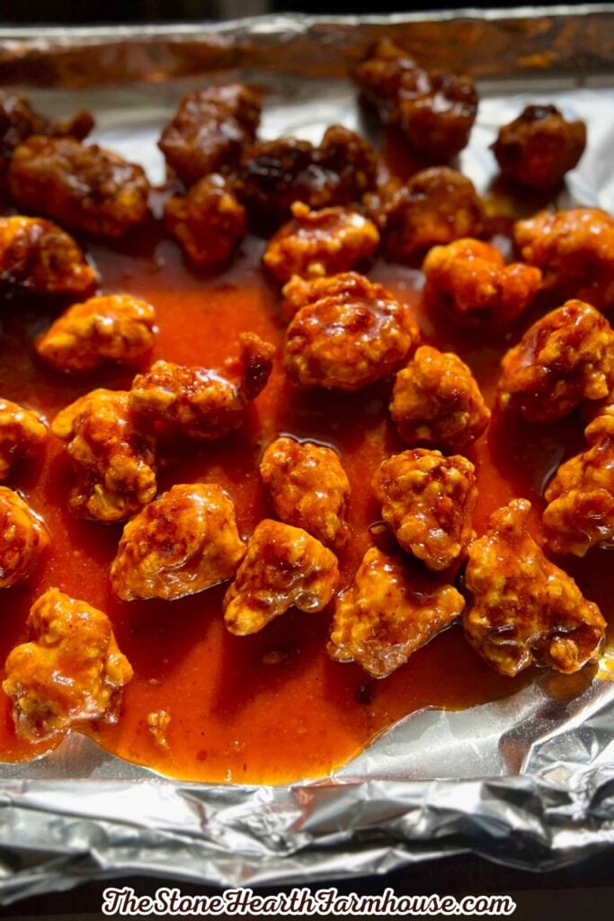 Crispy pieces of rabbit coated in a glossy spicy firecracker sauce on a baking sheet