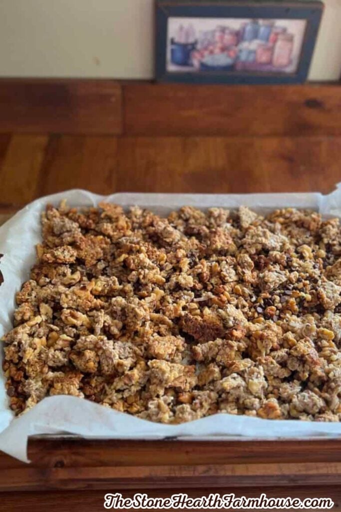 Freshly baked sourdough discard granola with oats, chopped nuts, and chocolate chips spread across a parchment-lined baking pan
