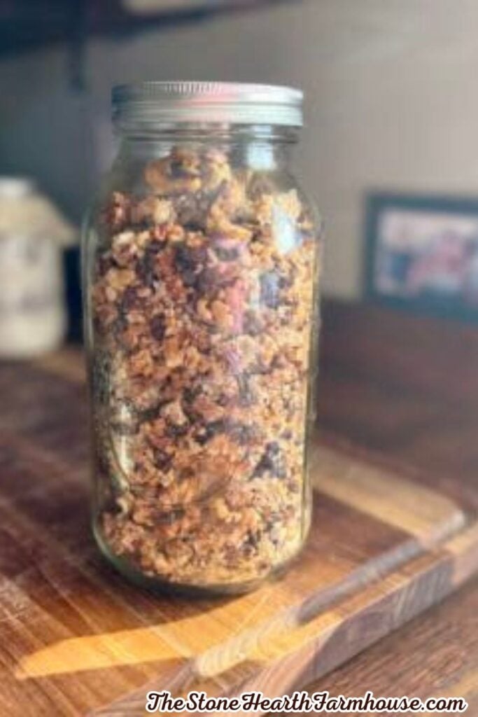 Homemade sourdough discard granola stored in a glass mason jar, showing crunchy clusters with oats, nuts, and chocolate chips on a wooden countertop.