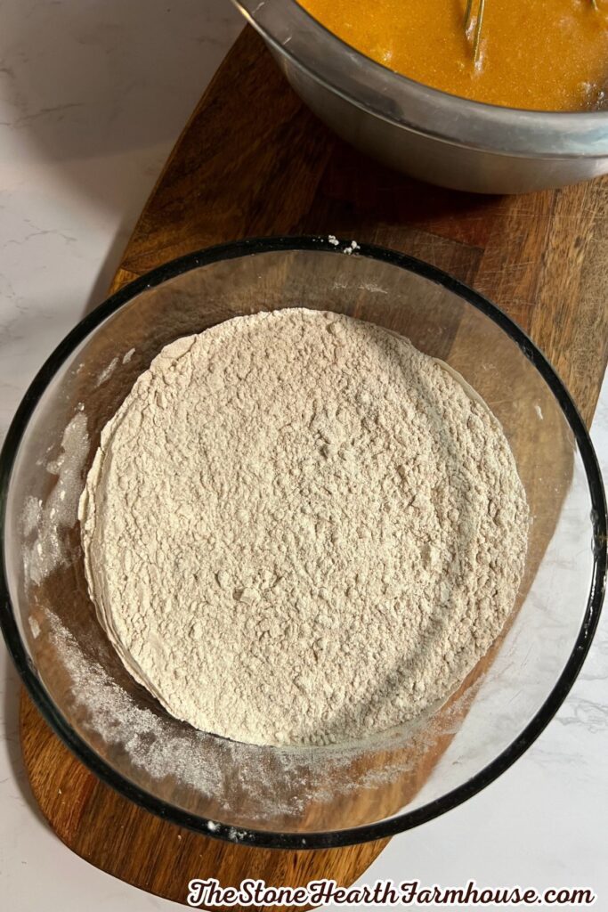 Flour mixture measured in a glass bowl with pumpkin spice and other dry ingredients prepared for baking.