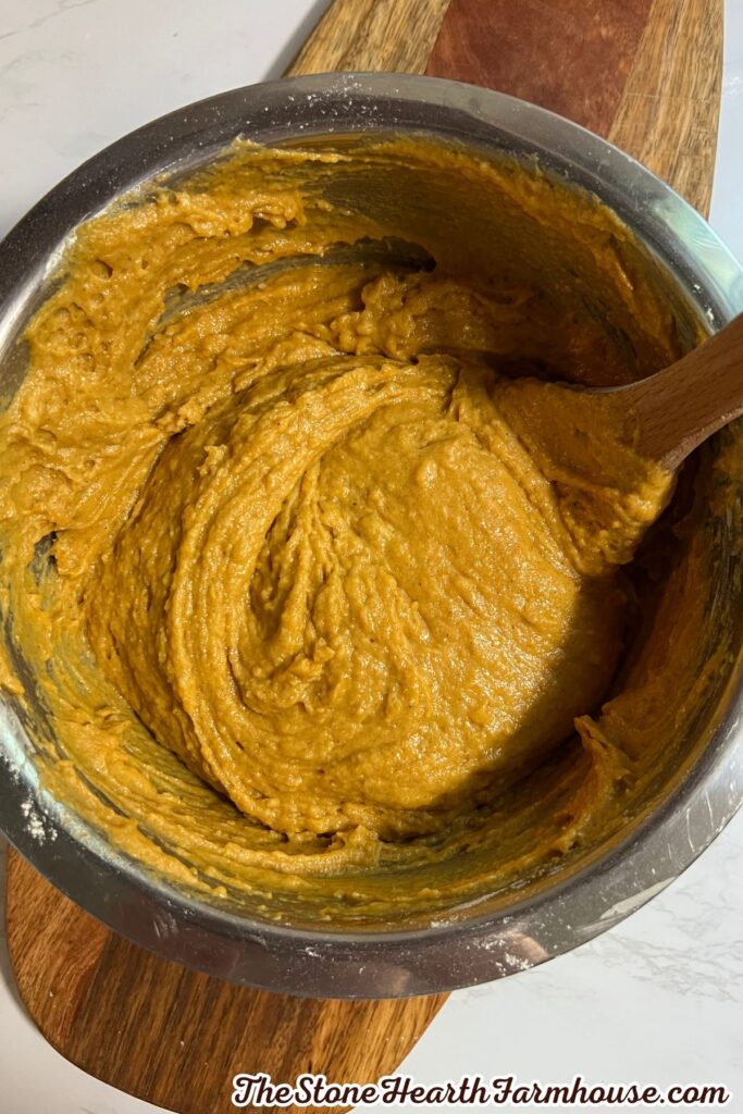 Thick pumpkin bread batter being stirred in a stainless steel mixing bowl with a wooden spoon.