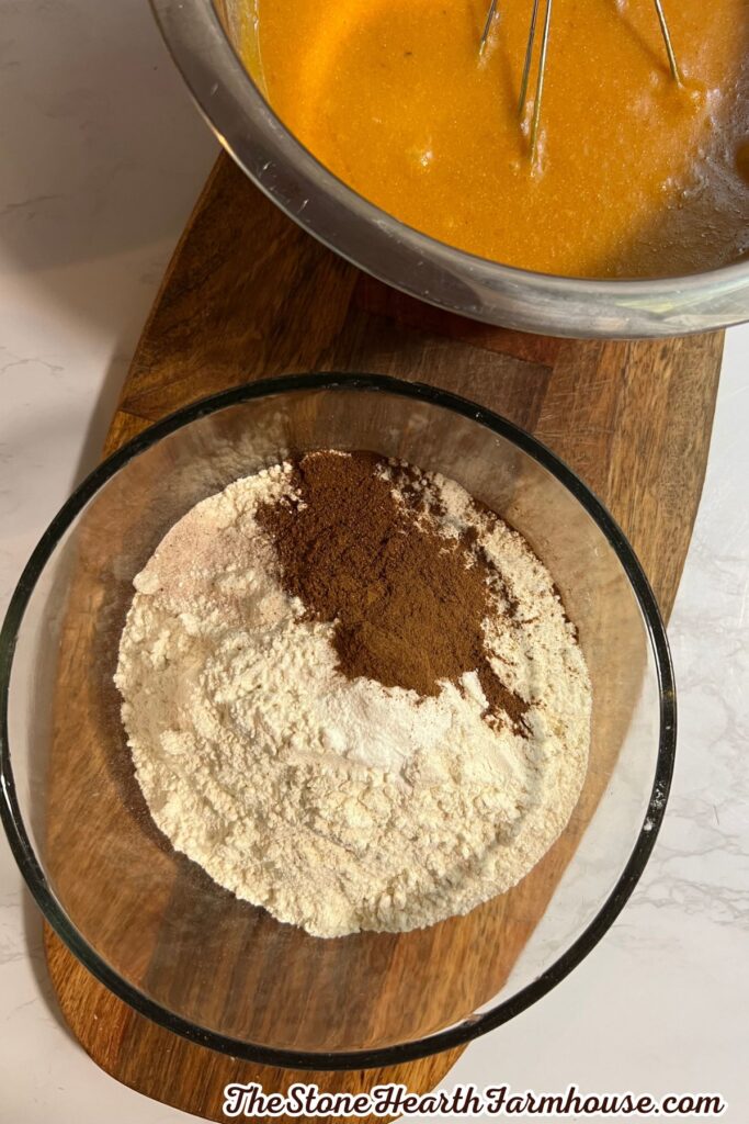 Dry ingredients including flour and pumpkin spice measured in a glass bowl beside pumpkin mixture in a mixing bowl.