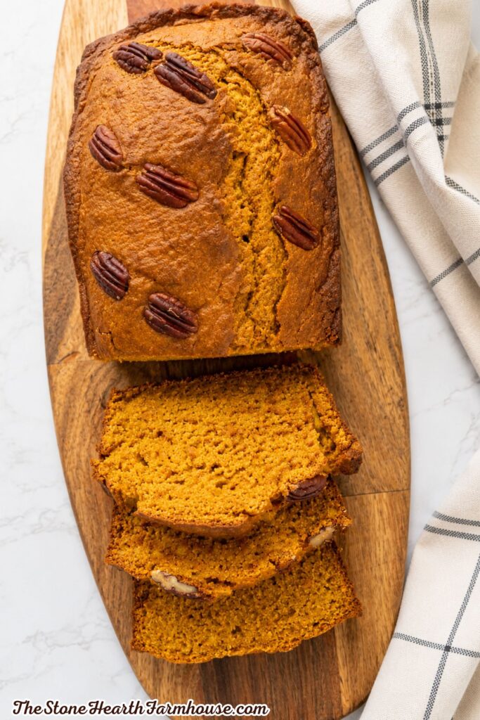 Freshly baked pumpkin bread with pecans sliced and stacked on a rustic wooden cutting board.