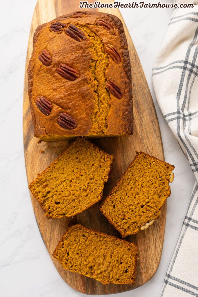 Homemade pumpkin bread loaf topped with pecans and several thick slices arranged on a wooden serving board.