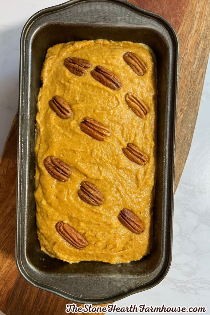 Unbaked pumpkin bread batter in a loaf pan topped with pecan halves and ready for the oven.