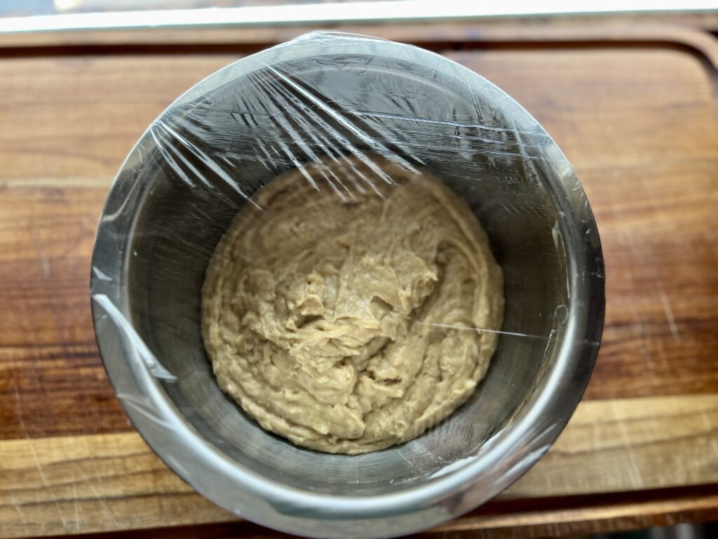 a bowl of bread batter covered with plastic wrap and ready to ferment.