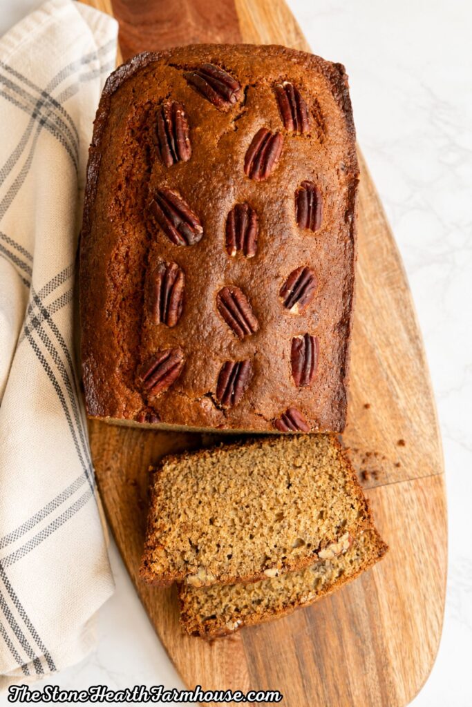 Moist homemade banana bread with pecans sliced on a wooden farmhouse cutting board