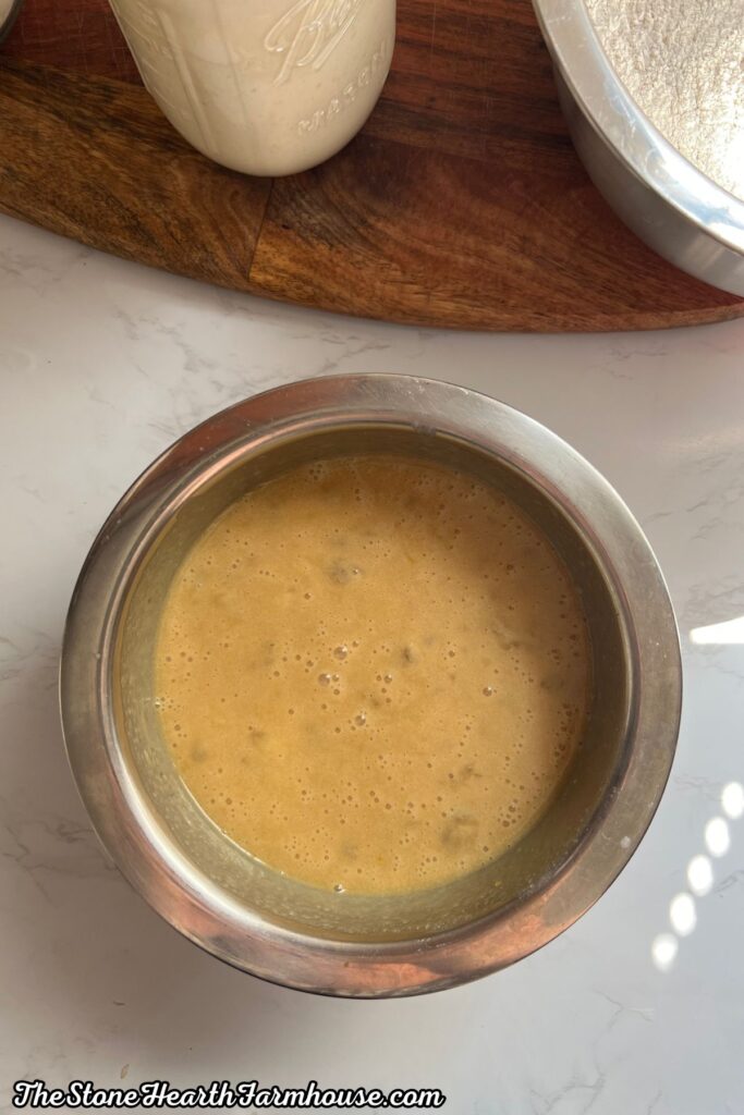 Wet banana bread ingredients combined in a mixing bowl adding in mashed bananas. 