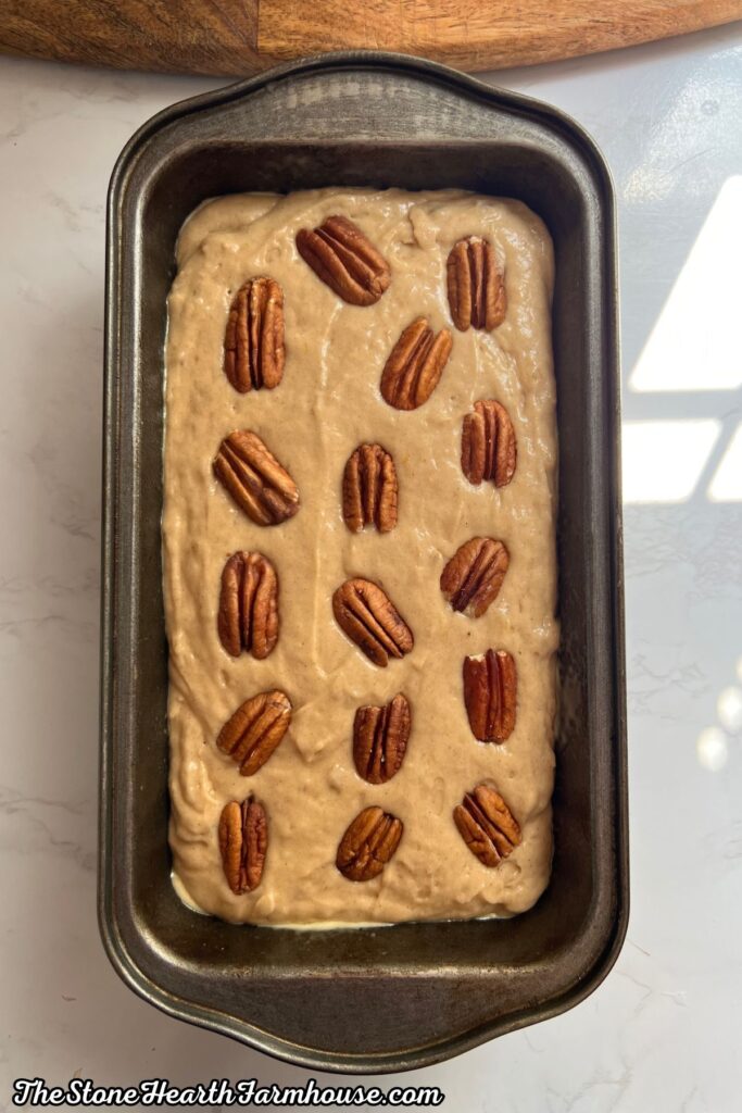 Alt text: Banana bread batter topped with whole pecan halves arranged across the loaf before baking