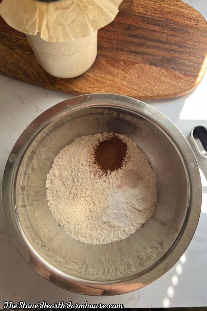 Dry ingredients for banana bread measured in a stainless steel mixing bowl with flour, cinnamon, and baking soda
