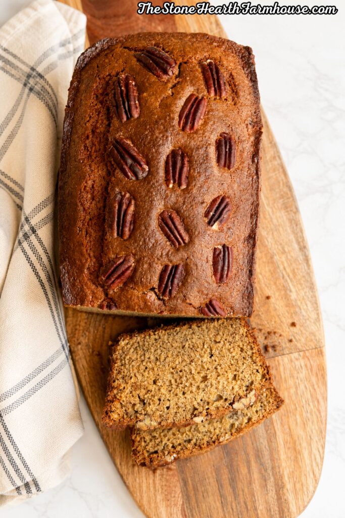 Sourdough discard banana bread topped with pecans and sliced on a wooden farmhouse cutting board