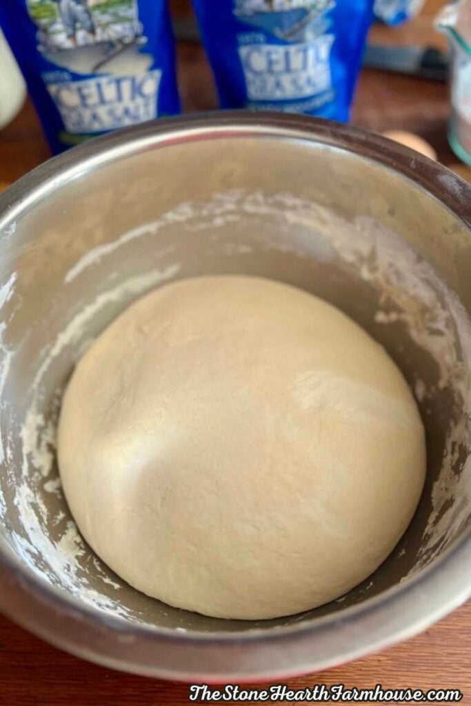 Smooth ball of pretzel dough resting in a stainless steel mixing bowl