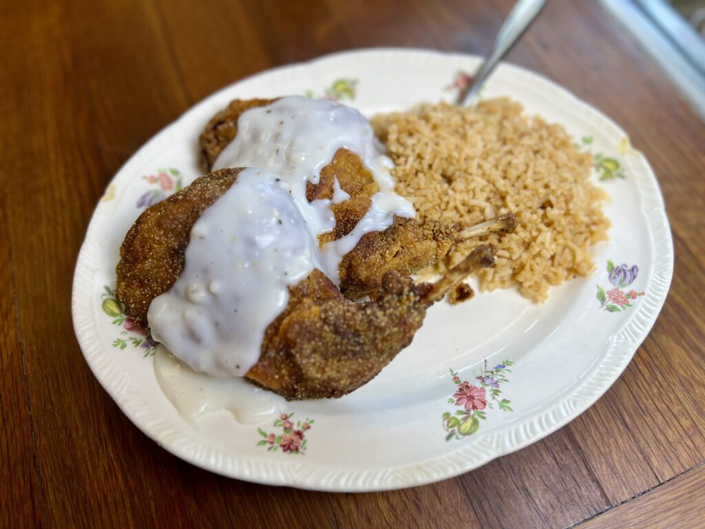 Fried rabbit on a white plate with flowers. Served with rice and white country gravy.