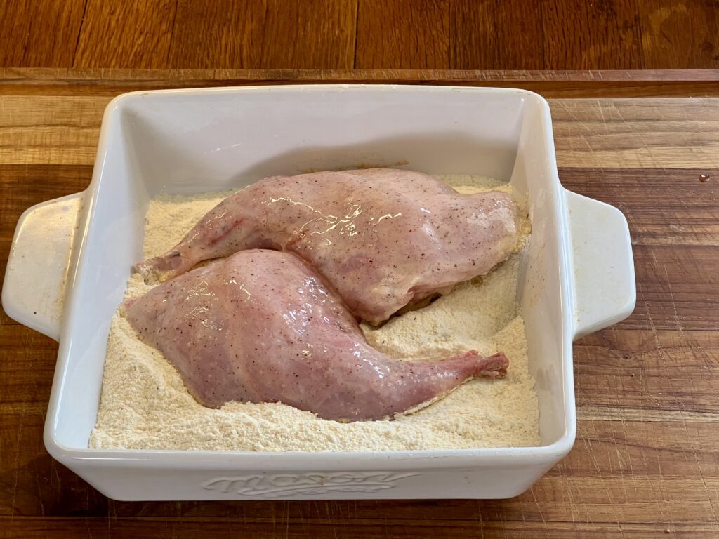 Rabbit thighs in a white square dish ready to be coated in the breading.