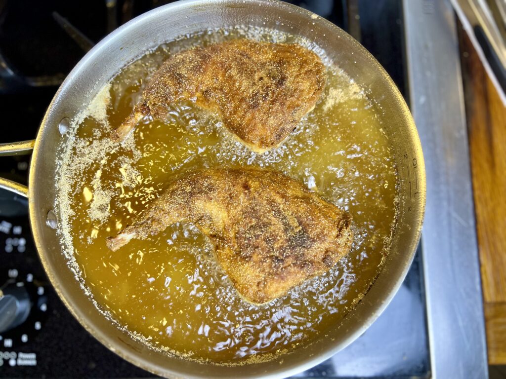 Rabbit thighs frying in a stainless steel pan on the stove.
