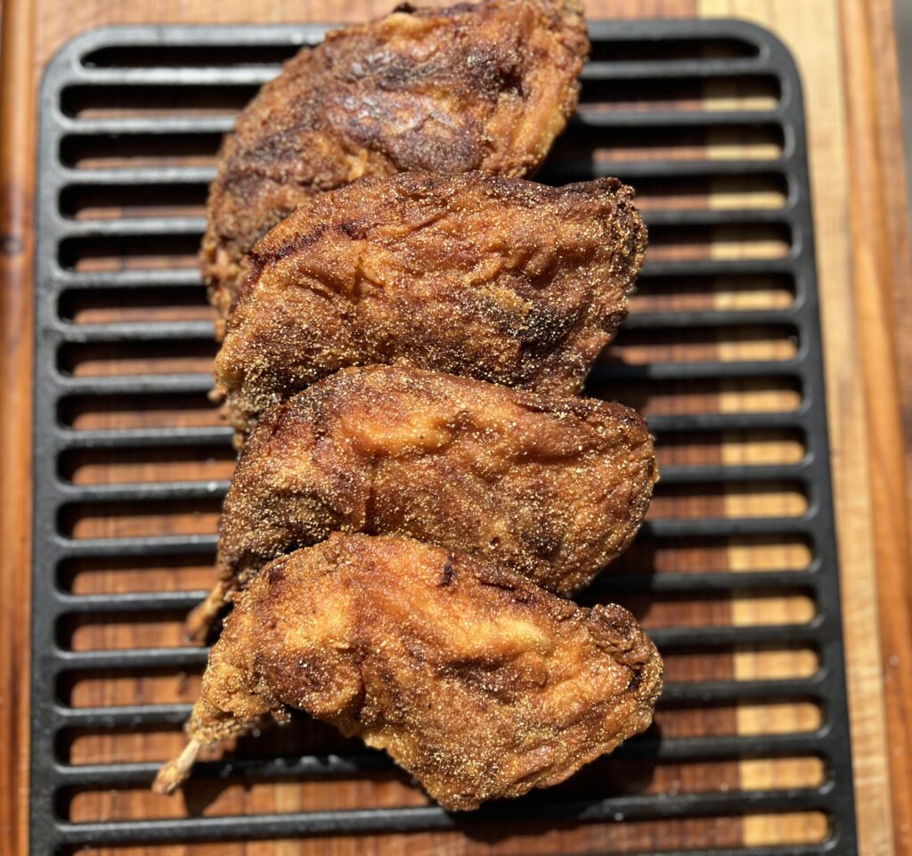 Crispy golden brown fried rabbit pieces resting on a black cooling rack over a wooden cutting board, perfectly seasoned and cooked for a Southern-style meal