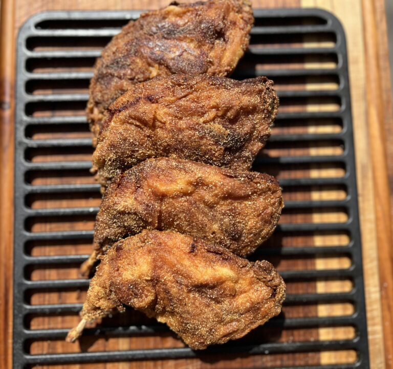 Crispy golden brown fried rabbit pieces resting on a black cooling rack over a wooden cutting board, perfectly seasoned and cooked for a Southern-style meal