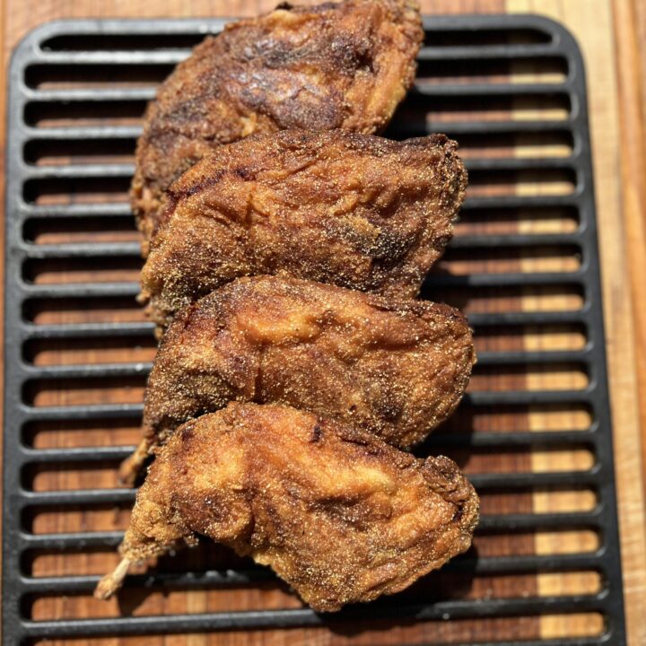 Crispy golden brown fried rabbit pieces resting on a black cooling rack over a wooden cutting board, perfectly seasoned and cooked for a Southern-style meal