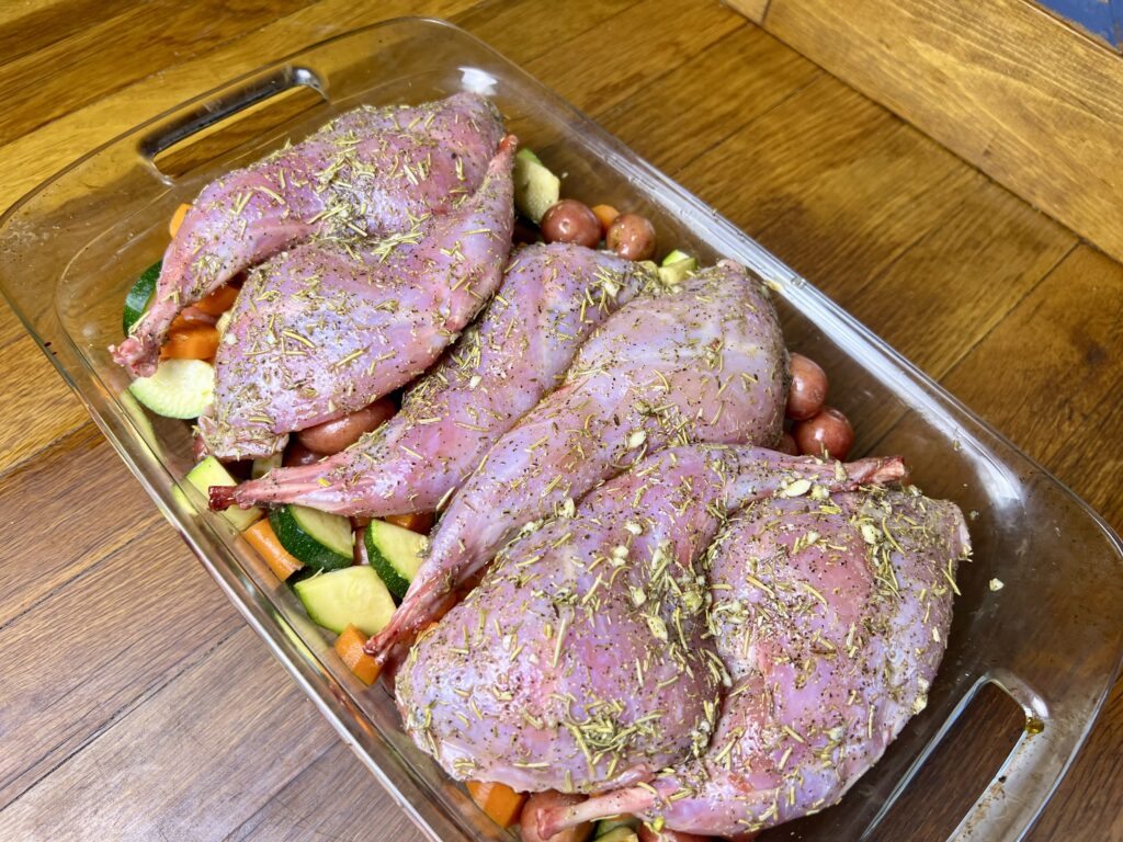 uncooked rabbot thighs in a baking dish on top of vegetables.
