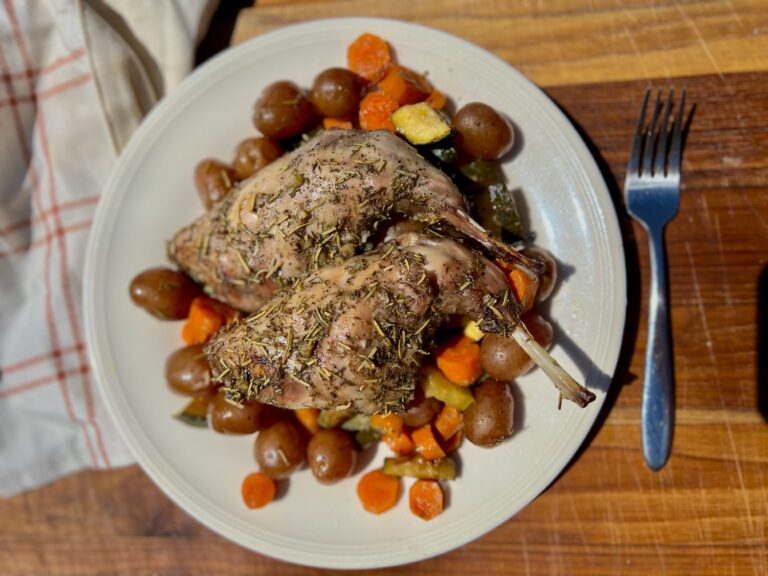 a plate of roasted rabbit on top of roasted vegetables, carrots, baby potatoes