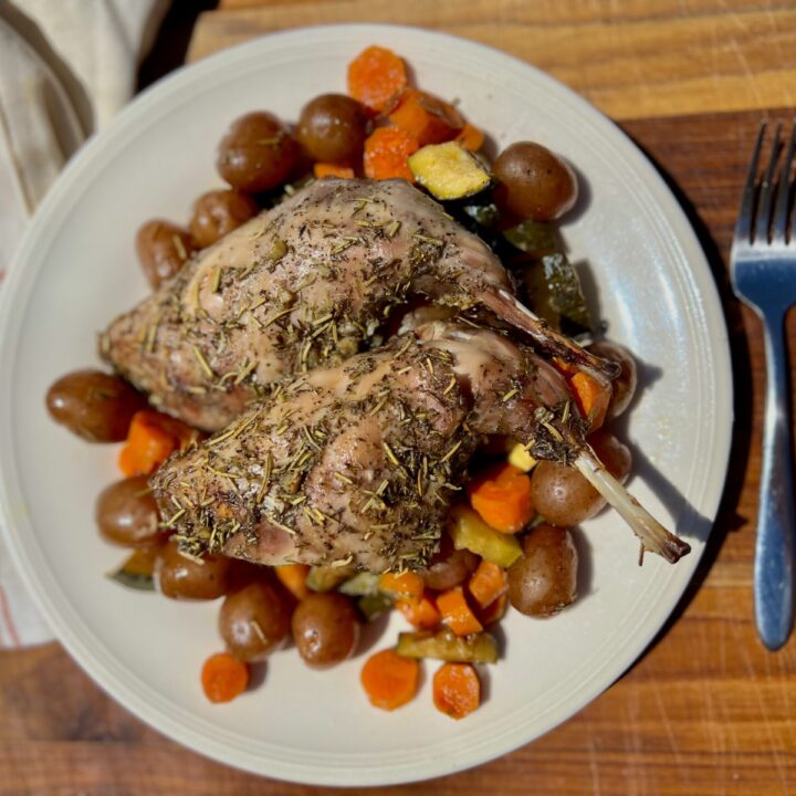 a plate of roasted rabbit on top of roasted vegetables, carrots, baby potatoes