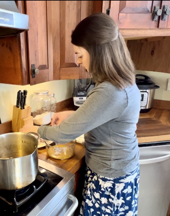 a women in her kitchen at the stove preparing rabbit meat in an egg wash to fry.