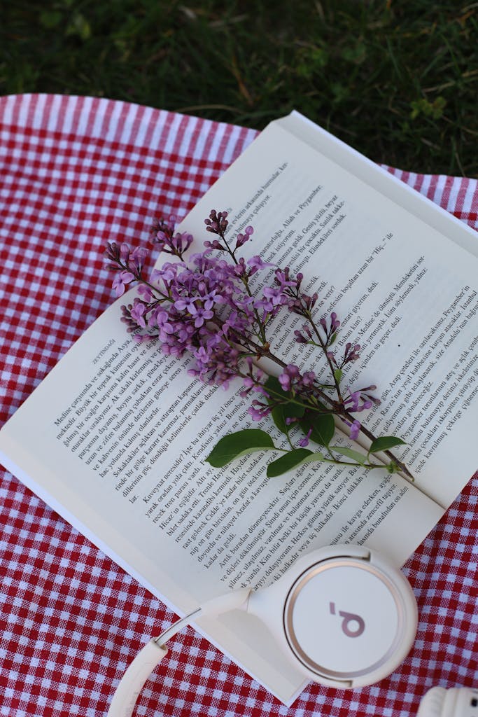 Open book and lilac flowers on a picnic blanket, serene outdoor scene.