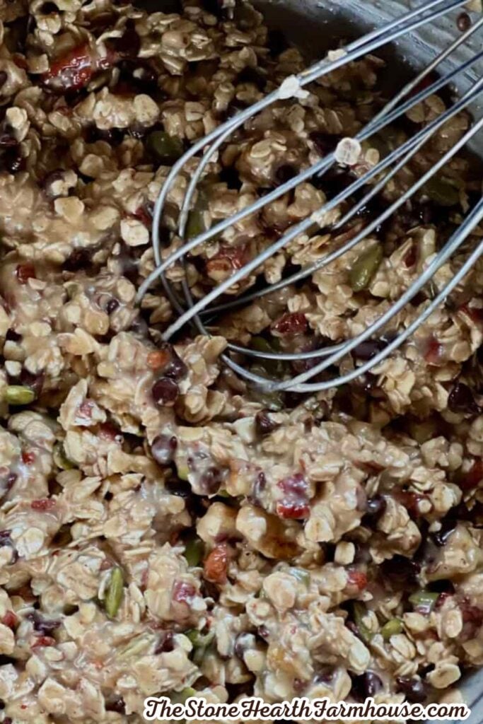 Oat and chocolate chip granola mixture with pumpkin seeds and nuts being stirred with a whisk