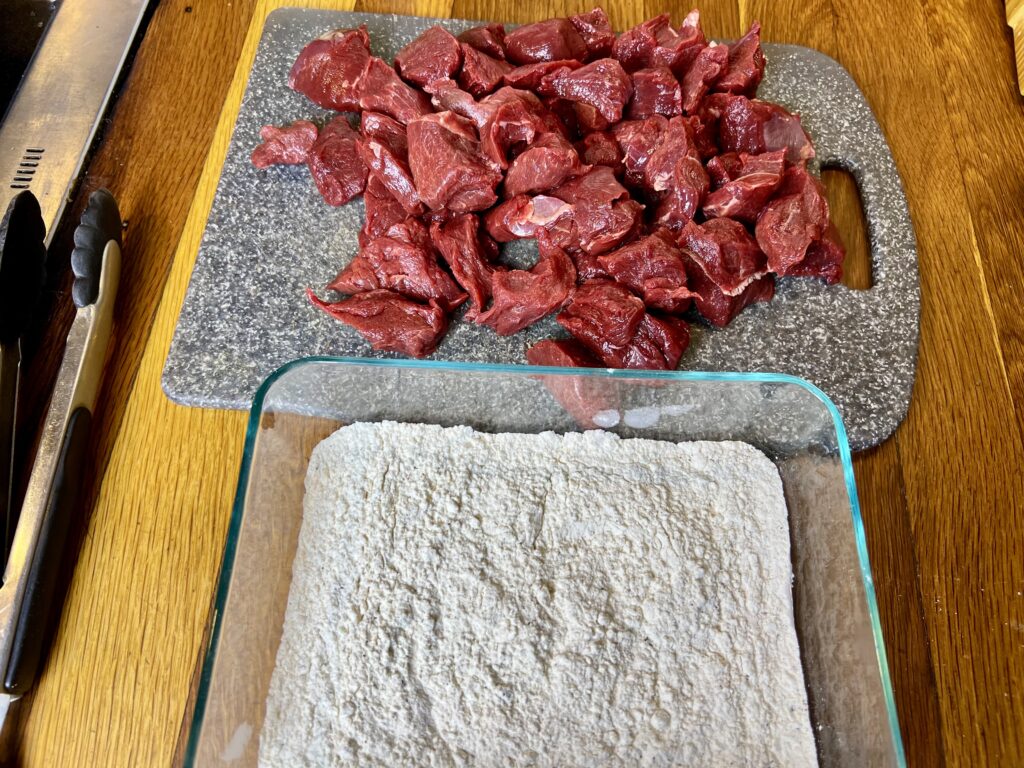 Venison stew meat on a cutting board ready to go into a flour mixture.
