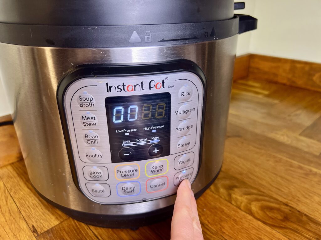 A hand pressing the pressure cook button on the instant pot.