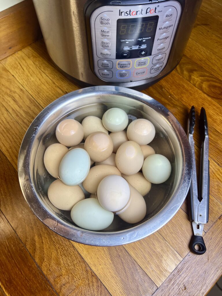Freshly cooked farm eggs in an ice water bath after being hard boiled in an Instant Pot, with tongs and the pressure cooker nearby.