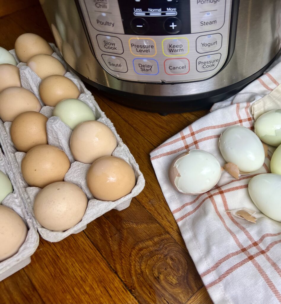 partially cracked hard boiled eggs next to a carton of fresh eggs and a instant pot in the back round.
