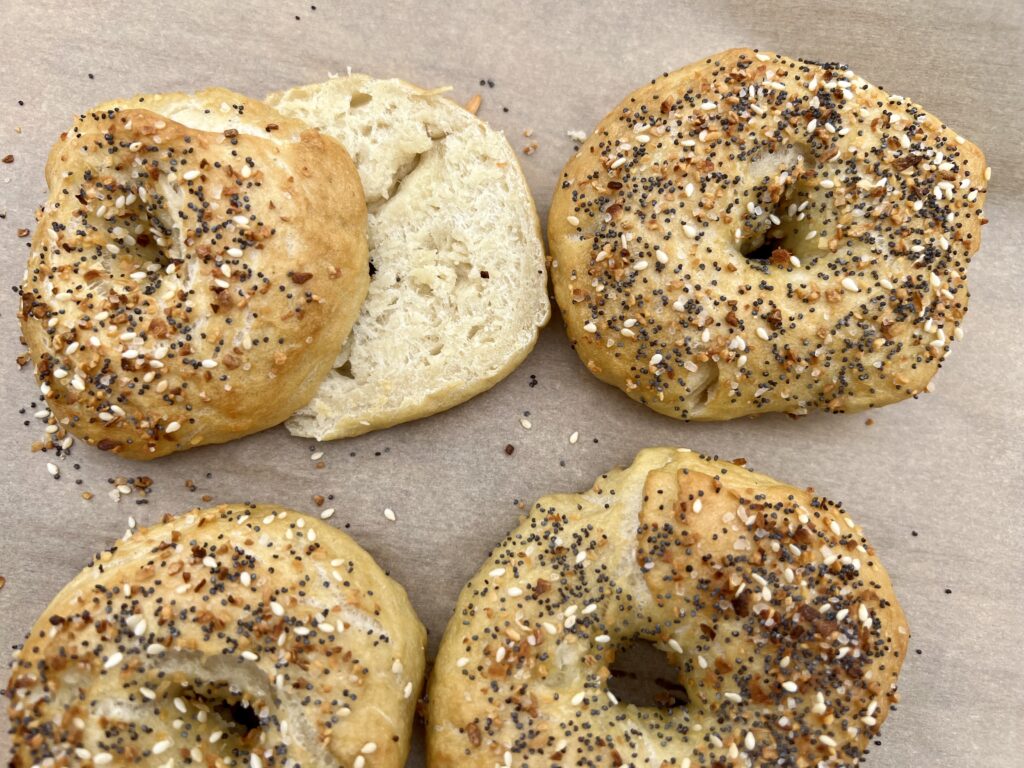 4 sourdough bagels up close on parchment paper with everything bagels seasoning. One is sliced in half.