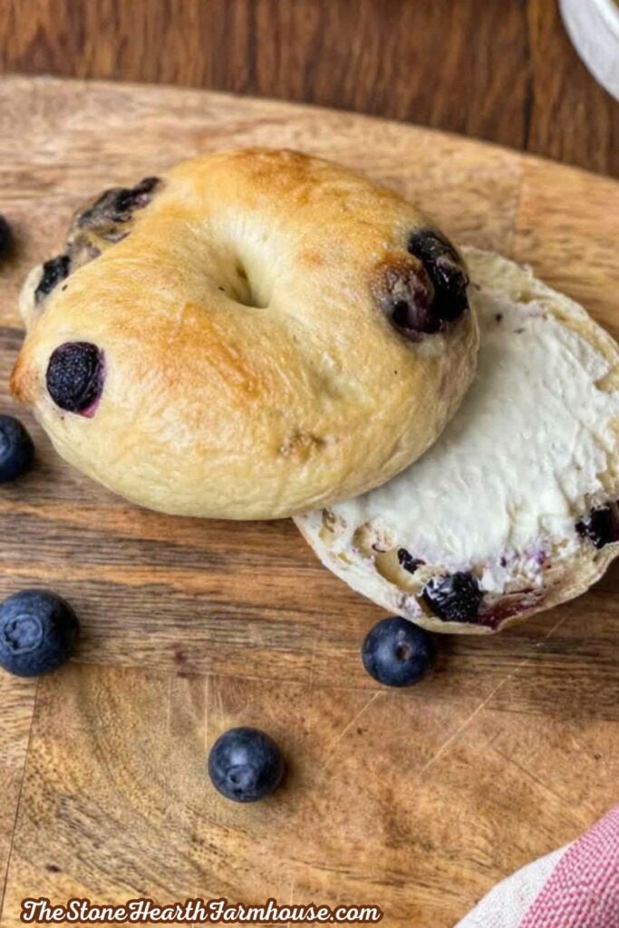 Freshly baked sourdough blueberry bagel sliced open and served with cream cheese on a wooden cutting board