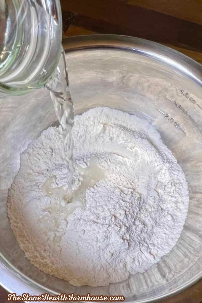 Water being poured into flour mixture while preparing homemade sourdough blueberry bagel dough
